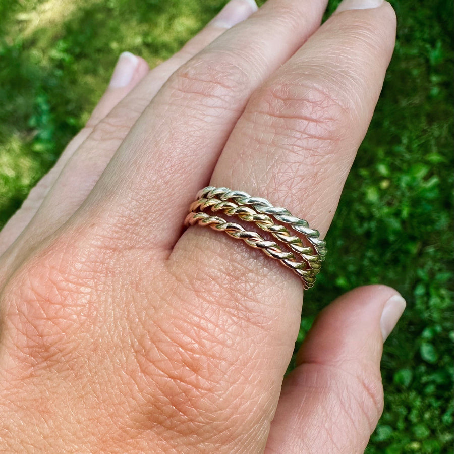 Hand wearing three stacking rings with a green grass background