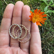 Hand holding three rings with a small orange flower in front of grass